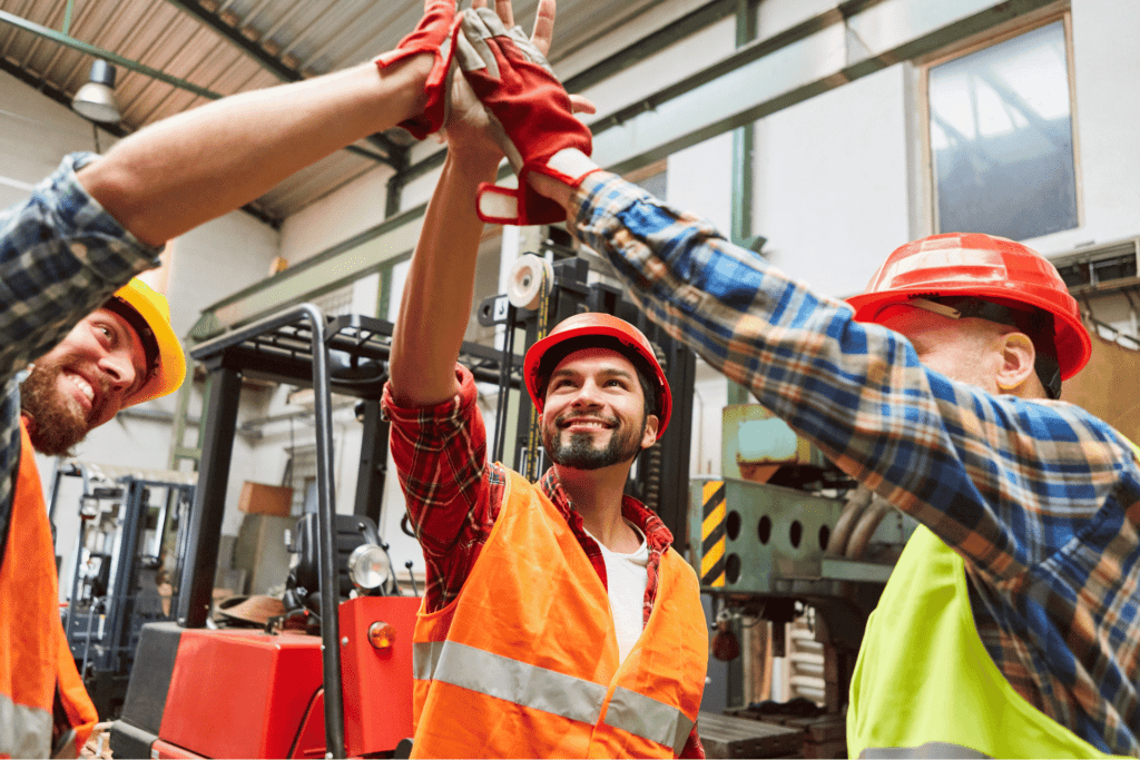 Team of workers in safety gear celebrating in a 3PL warehouse in Newark, NJ, a hub for logistics and customs clearance near NYC.